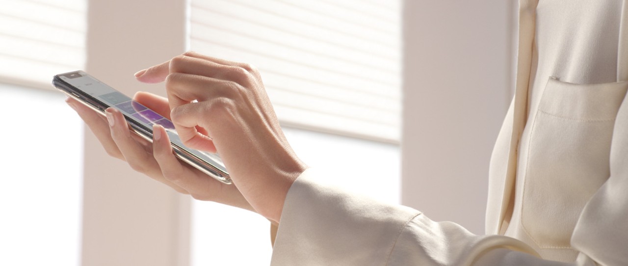 Women holding a phone controlling her Sonnette® Cellular Roller Shades with PowerView® Automation.